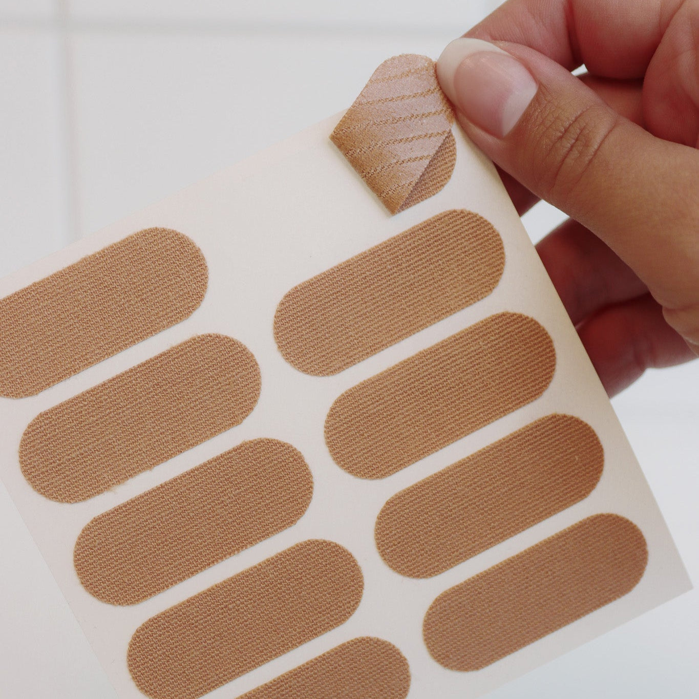 Hand holding a HOLLI kinesiology face tape sheet of pre-cut patches on a white background