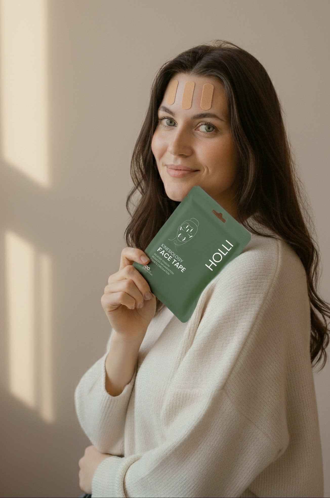 Woman holding a green HOLLI Pre-cut Face Taping Kit against a neutral background