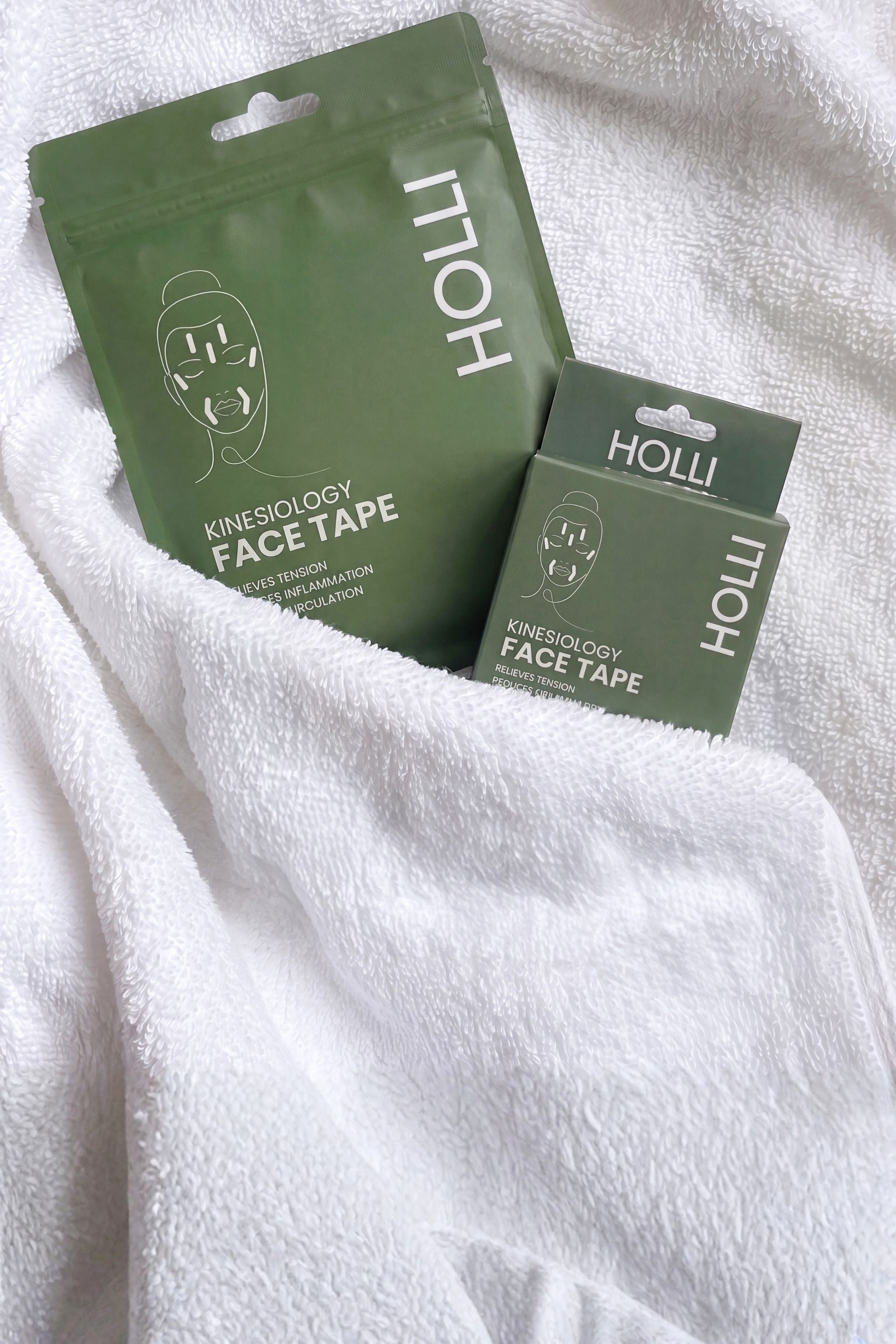 Two green HOLLI Kinesiology Face Tape pouches resting on a white textured towel.